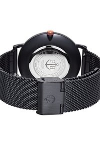 Orologio con cinturino in rete nera, cassa rotonda nera, corona in ottone, retro trasparente che mostra il logo e dettagli argentati sul quadrante.