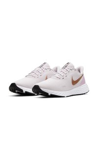 Scarpe da corsa Nike in rete rosa chiaro con swoosh bronzo, suola intermedia bianca e suola esterna in gomma nera; presenta una superficie testurizzata e un design con lacci.
