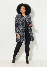 Cardigan à motif noir et blanc, à manches longues, ouvert sur le devant, associé à des leggings noirs et des bottines. Texture lisse, motif floral.