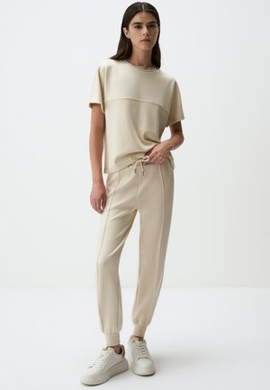 Ensemble de loisirs beige comprenant un haut à manches courtes avec des coutures et un pantalon à coupe décontractée avec une taille élastique et des poignets effilés.