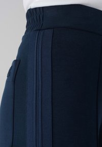 Marineblauwe joggingbroek met een elastische tailleband, voorzien van drie gep textured strepen aan de zijkant en een klein zakje op de linkse heup.