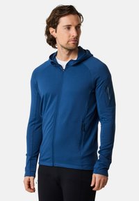 Felpa blu con zip, realizzata in un tessuto testurizzato, con cappuccio regolabile e tasca con zip sul braccio sinistro. Vestibilità aderente con maniche lunghe.