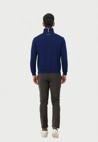 Navy quarter-zip sweatshirt with a high collar, ribbed cuffs, and hem. Paired with dark grey pants and white sneakers with green accents.