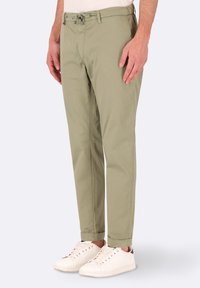 Chinos verde oliva chiaro con un fit slim, vita con cordoncino, tasche frontali e orli arrotolati, abbinati a sneakers bianche.