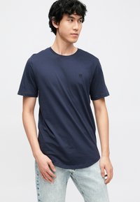 Camiseta de algodón azul marino con cuello redondo, mangas cortas y un pequeño logo negro en el pecho. Textura suave y lisa.