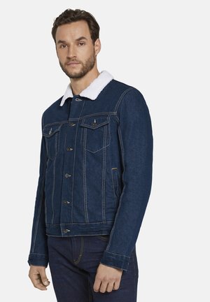 Denim jacket features dark blue fabric, white sherpa collar, two chest pockets, button-up front, and contrasting stitching details.