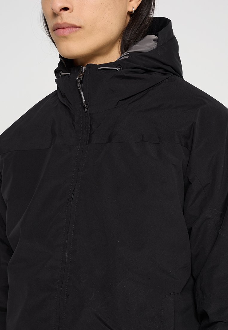 Giacca nera impermeabile con cappuccio, dotata di un colletto alto, chiusura con zip e tessuto leggero. Include dettagli con cordino sul cappuccio.