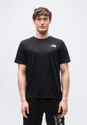 Fiatal férfi áll szemben, fekete The North Face pólót és hozzáillő, fekete rövidnadrágot visel grafikus logókkal.