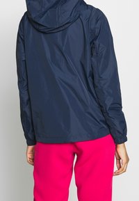 Granatowa, lekka kurtka z kapturem, elastycznymi mankietami i lekko zwężającym się pasem, zestawiona z jaskraworóżowymi spodniami.