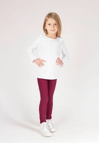 Biały top z długim rękawem i marszczonym dekoltem, zestawiony z bordowymi legginsami i białymi trampkami. Strój charakteryzuje się prostym, czystym designem.