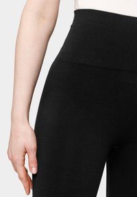 Černé žebrované legíny s vysokým páskem, vyrobené z elastického materiálu. Detailní záběr ukazující texturu a přiléhavost kolem pasu a oblasti boků.