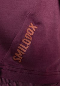 T-shirt de sport bourgogne avec une texture lisse et un logo "SMILODOX" imprimé sur le côté. Comprend des détails de couture sur l'ourlet.