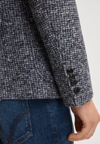 Blazer a fantasia blu navy e grigio realizzato in tessuto strutturato, con quattro bottoni neri sul polsino e design aderente.