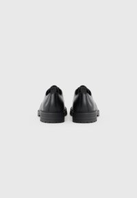 Zapatos de cuero negros con textura suave, puntera redonda y suela baja de goma, que cuentan con un diseño de costura sutil y una lengüeta en la parte trasera.