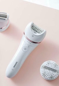 Épilateur Philips avec une poignée en plastique blanc, des accents roses, une tête striée pour l'épilation, et un embout texturé amovible pour le nettoyage.