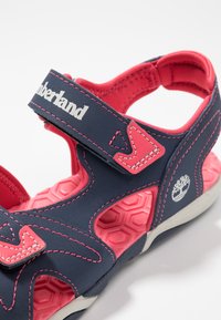 Navy and pink sandal with adjustable strap, hexagonal textured sole, and logo detail. Made from synthetic material, featuring stitched accents.
