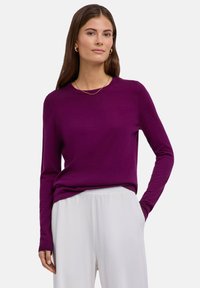 Maglione viola a maniche lunghe in tessuto liscio, scollatura rotonda, maniche aderenti, abbinato a pantaloni bianchi larghi.