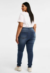 Mörkblå skinny jeans med bakfickor, hög midja och subtila sömnadsdetaljer, i kombination med en enkel ljusrosa t-shirt och vita sneakers.