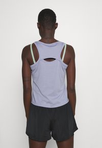 Camiseta sin mangas de color púrpura claro con un detalle de corte en la espalda, combinada con pantalones cortos negros; la tela parece suave y ligeramente ajustada.