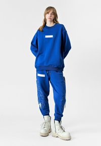 Sudadera azul y joggers a juego con bordado de alas, tejido texturizado y un acento de hardware rectangular en el bolsillo frontal.