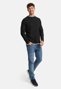 Suéter gris de punto con cuello redondo, combinado con jeans azul claro y zapatillas navy. El conjunto cuenta con una camiseta blanca de capa debajo.