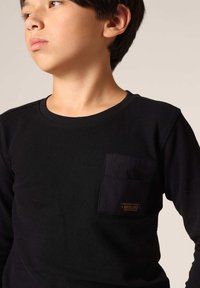 Zwart shirt met lange mouwen in ribbelstructuur, voorzien van een patchzak op de linkerborst met een klein logo-label.