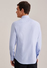 Camicia azzurra chiara a maniche lunghe con colletto strutturato, polsini con bottoni e un sottile motivo a righe. La vista posteriore mostra l'orlo curvato e una vestibilità sagomata.