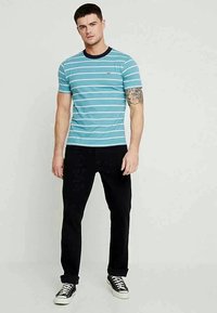 Tricou cu dungi albastre și guler bleumarin, din material de bumbac, asortat cu pantaloni negri și adidași negri. Are un logo mic pe piept.