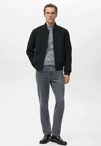 Chaqueta bomber negra de tela suave, suéter de punto gris con patrón de diamantes debajo, jeans grises y botas negras hasta el tobillo. Diseño simple.