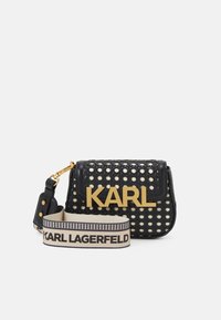 Bolso de hombro de tejido negro con un gran "KARL" dorado en la solapa y una correa ajustable beige con la marca "KARL LAGERFELD" en texto negro.