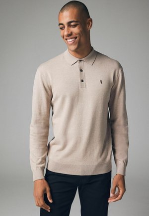 Beige Langarm-Polohemd mit drei dunklen Knöpfen, strukturiertem Stoff, gerippten Bündchen und Saum, mit einem kleinen Logo auf der linken Brust.
