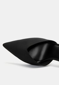 Black pointed-toe pump with a smooth texture and an open cut-out design. Features a sleek silhouette and a solid, matte finish.