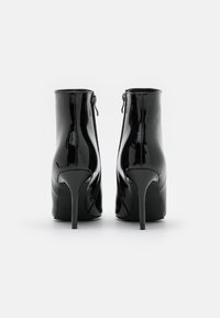 Bottines en cuir verni noir avec un talon stiletto haut et une fermeture éclair à l'arrière, présentant une texture lisse et brillante.