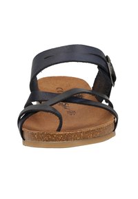 Sort lædersandal med krydsremme, brun korksål og en lille metalspændeaccent på siden. Flad sål.