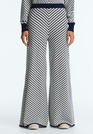 Nohavice s širokými nohavicami s diagonálnymi námorníckymi a bielymi pruhmi, doplnené o zodpovedajúci top s dlhým rukávom a biele topánky.