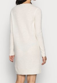Robe tricotée à manches longues de couleur crème avec une coupe droite. Texture douce, col rond et détail le long de l'ourlet.