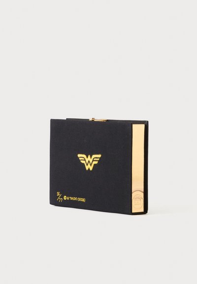 Pochette rectangulaire noire avec logo Wonder Woman doré, détail de bord doré et marquage d'édition numérotée sur fond clair.