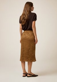 Brun stickad topp i kombination med en knälång spetskjol i en rik gyllene nyans, med intrikata blommönster och en mjuk textur.