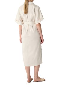 Beige Hemdkleid mit kurzen Ärmeln, tailliertem Gürtel und seitlichen Taschen. Glattes Material, knielanger Saum und kombiniert mit flachen Schuhen.