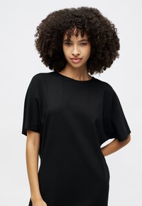 Black oversized t-shirt with short sleeves, round neckline, made from smooth fabric. Features a loose fit and minimalistic design.
