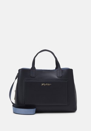 Sac à main en cuir noir avec deux poignées courtes, poche avant et bandoulière en tissu bleu amovible, sur fond blanc.