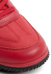 Scarpa sportiva rossa con una combinazione di pelle liscia e tessuto texture, punta arrotondata, design con lacci e suola in gomma nera testurizzata.