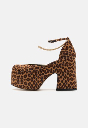 Leopard print platform heels with a thick block heel, ankle strap, and gold chain detail. Made from textured material.