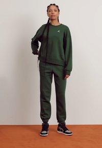 Groene sweatshirts en bijpassende joggers in een zachte stof. Met een klein wit logo op de borst en elastische manchetten op de broekspijpen. Zwarte sneakers.