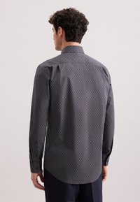 Camicia a maniche lunghe con un motivo scuro che presenta intricate geometrie in blu e bianco, colletto classico, taglio aderente e orlo curvo.
