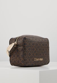 Borsa cosmetica Calvin Klein in faux leather marrone, con un motivo logo CK in rilievo, hardware dorato e chiusura con zip.