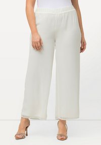 Wijdvallende broek in lichtcrème stof met een gladde textuur; heeft een elastische tailleband en valt tot op de enkel. Met een golvende zoomdetail.