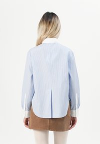 Light blue and white striped shirt with long sleeves, a back pleat, and white buttoned cuffs, worn with a brown skirt.