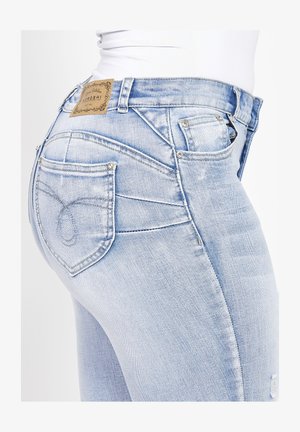 Světle modré džíny z denimu s texturovaným povrchem, se zakřiveným designem zadní kapsy a koženou nášivkou s logem na pase.