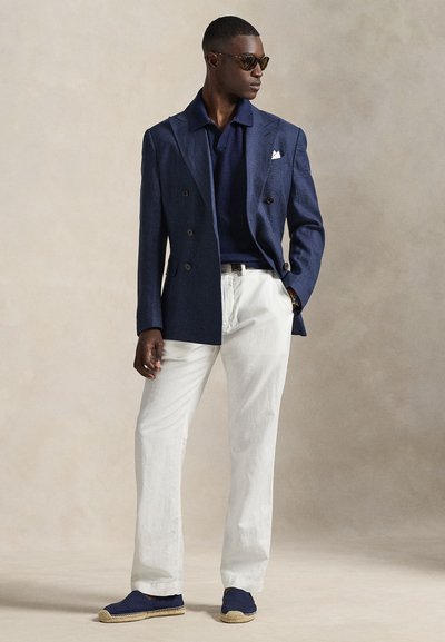 Μπλε διπλόστενο μπλέιζερ του πολεμικού ναυτικού πάνω από μπλε πόλο, λευκό λινό παντελόνι και μπλε εσπαντρίγιες με μπεζ σόλες. Συνοδεύεται από γυαλιά ηλίου.